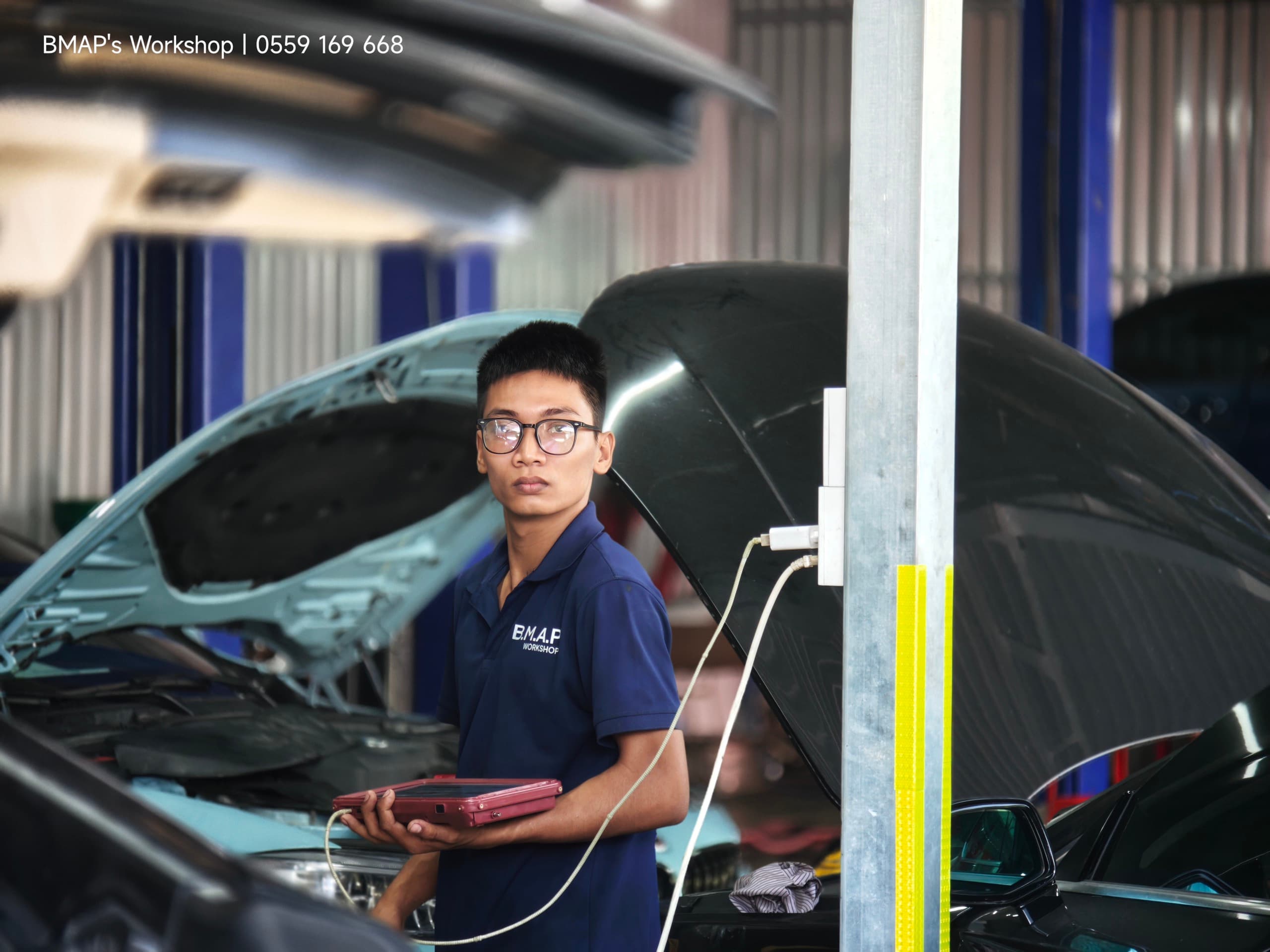 Dương Thành Vải — kỹ sư máy BMAP Workshop cầm máy chẩn đoán giữa hai xe đang mở khoang máy