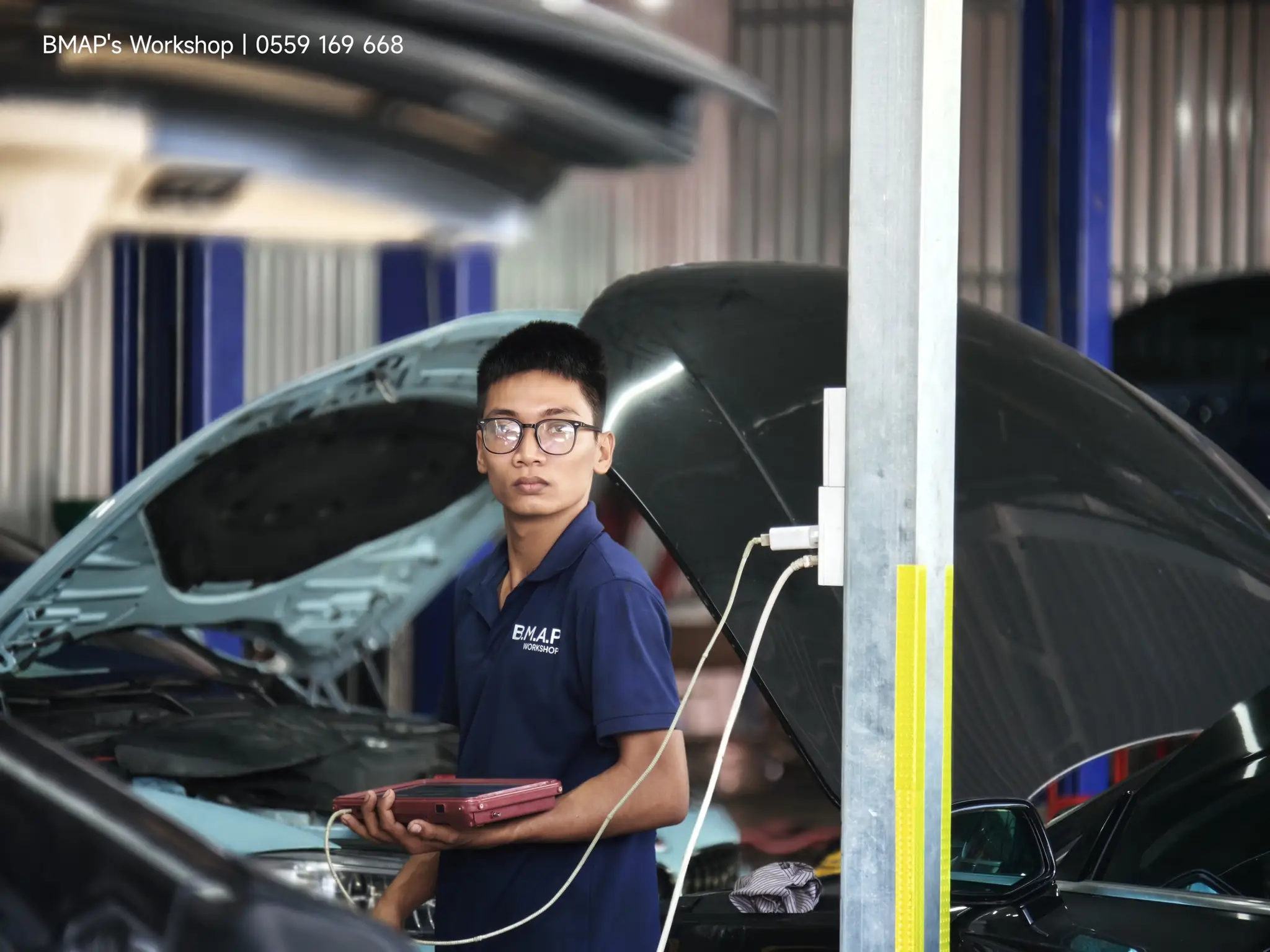 Dương Thành Vải — kỹ sư máy BMAP Workshop cầm máy chẩn đoán giữa hai xe đang mở khoang máy